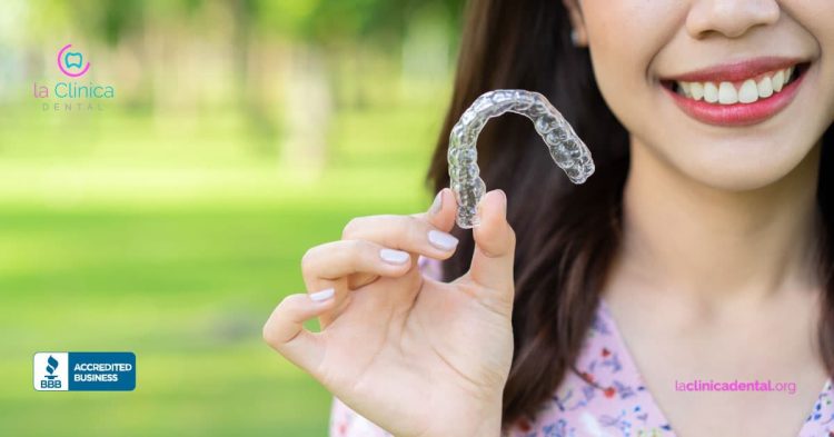 Mujer sonriente sosteniendo alineador dental transparente Invisalign en un entorno natural, destacando la innovación en tratamientos estéticos de La Clínica Dental.