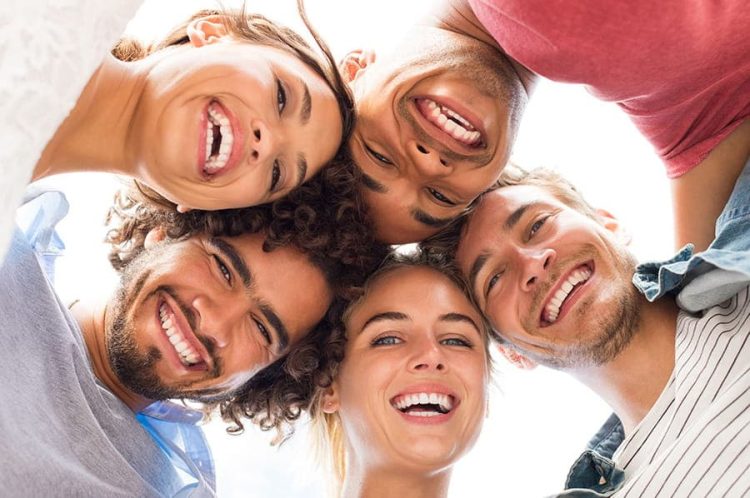 Grupo de personas sonriendo en círculo, destacando sonrisas saludables y felices, simbolizando la satisfacción con tratamientos estéticos dentales en La Clínica Dental.