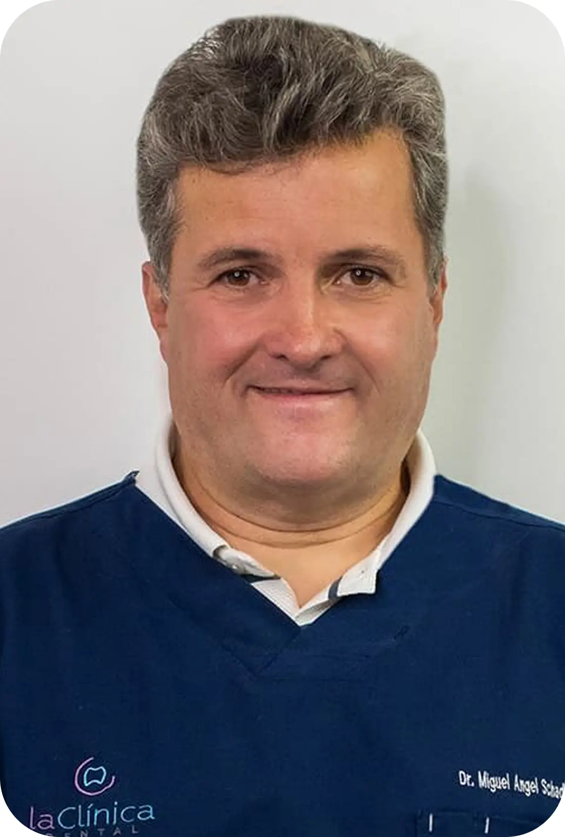 Dr. Miguel Ángel S., especialista en endodoncia, en La Clínica Dental Roma, con uniforme azul y logo de la clínica visible.