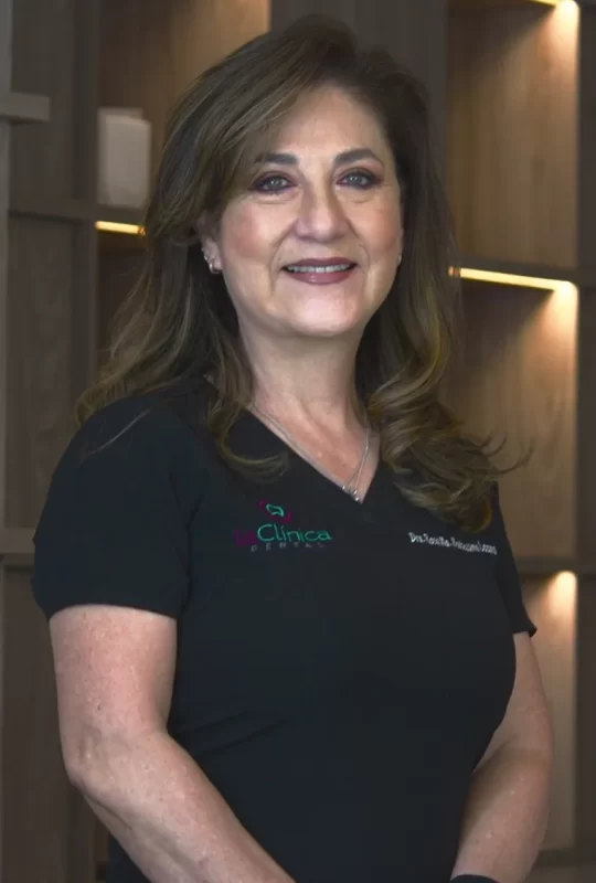 Dr. Hilda G., specialist in Maxillofacial Surgery at La Clínica Dental, smiling in a professional setting with modern decor.