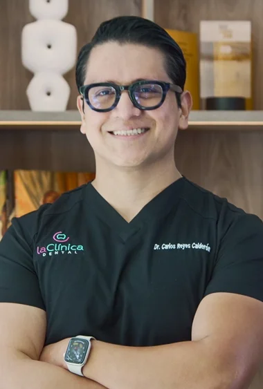 Dr. Carlos Reyes Calderón, dentist at La Clínica Dental, smiling in professional attire with clinic branding visible in the background.