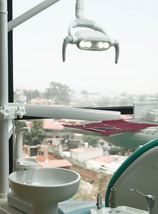 Dental clinic interior featuring modern dental equipment, including an overhead light, dental chair, and tools, with a view of the city skyline in the background, reflecting La Clínica Dental Roma’s commitment to advanced dental care.