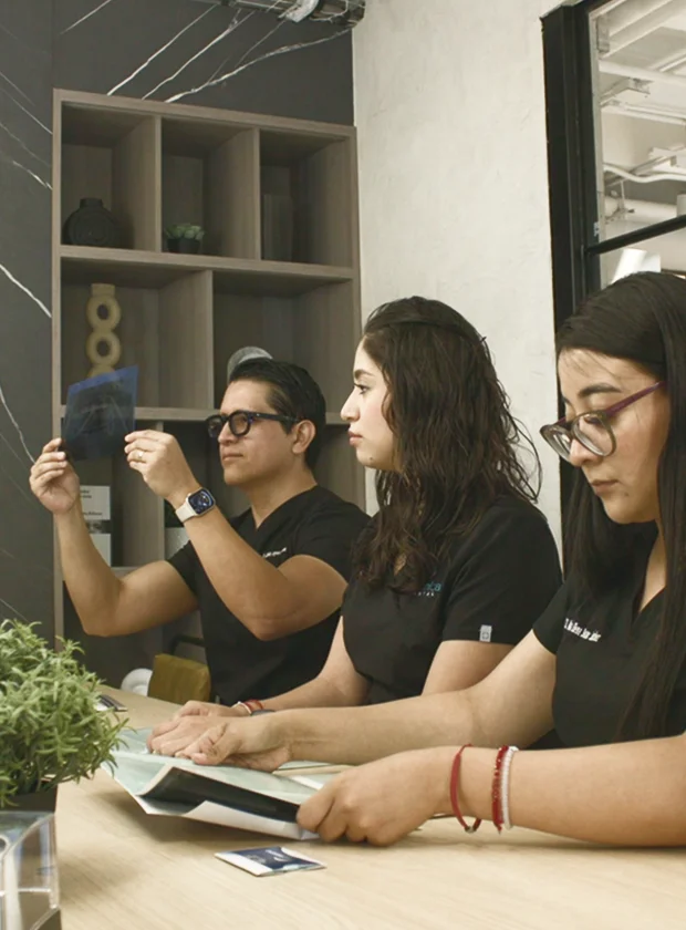 Team of dental professionals reviewing patient x-rays and documents in a modern clinic setting at La Clínica Dental Roma, showcasing commitment to advanced dental care and technology.