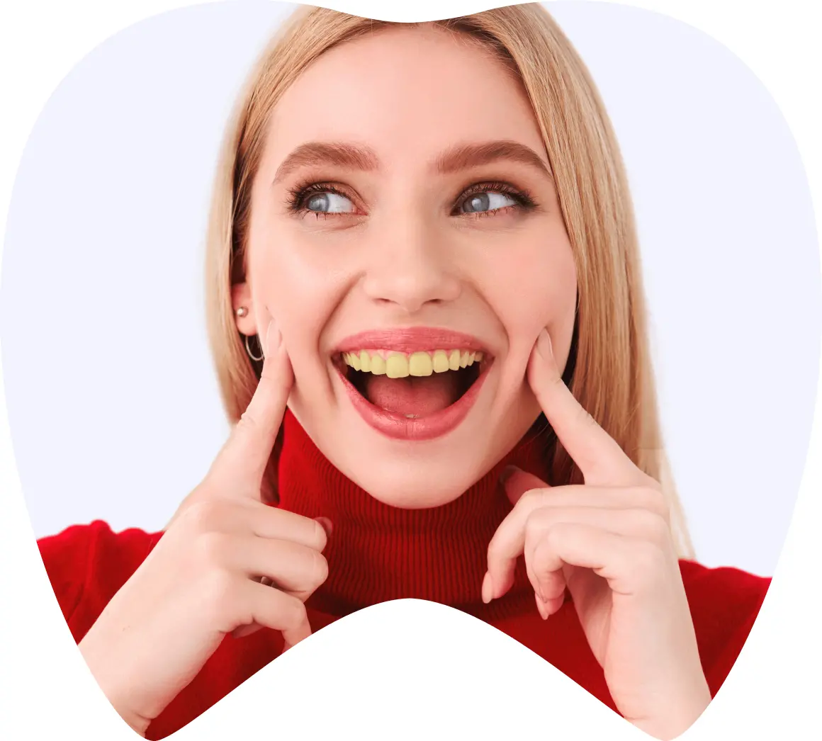 Mujer sonriendo con dientes amarillos, mostrando su sonrisa mientras se toca la mejilla, simbolizando la experiencia de turismo dental en La Clínica Dental Roma.